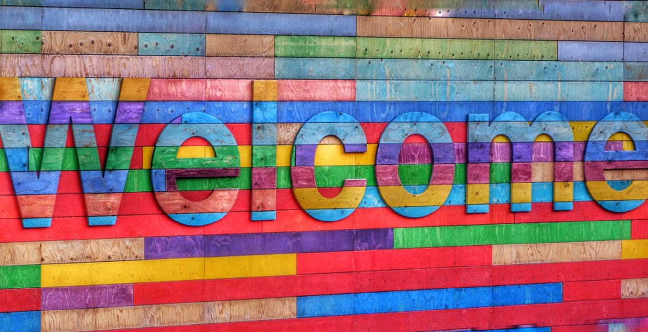welcome sign in rainbow colors on a wooden fence