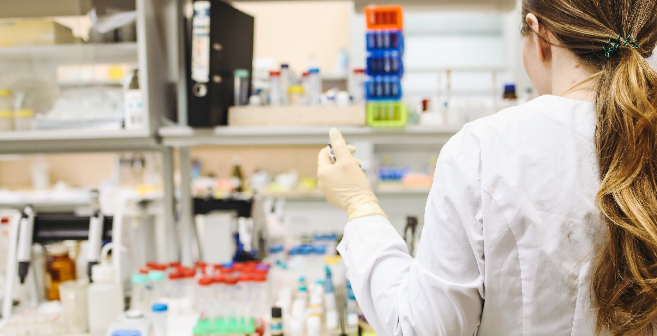 a shot from behind a researcher while they work at a lab space with alot of test tubes