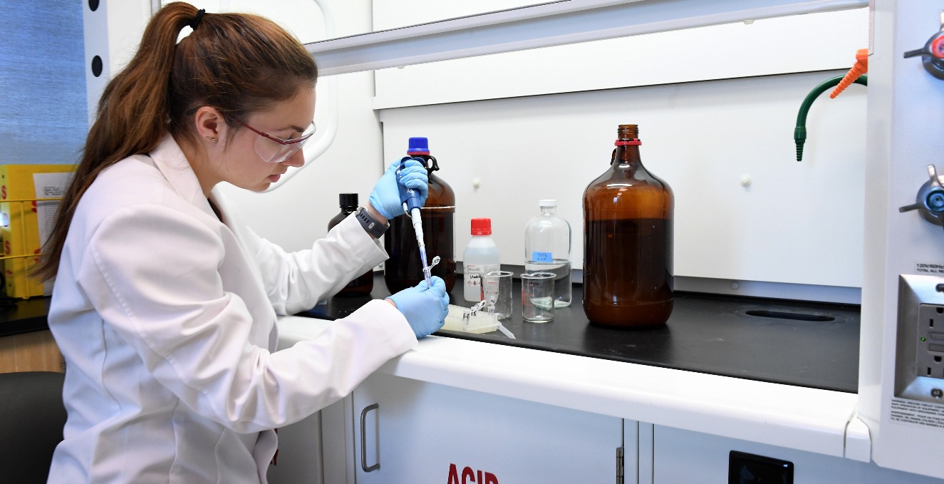 a researcher pumps liquid into a tube at a table in a lab